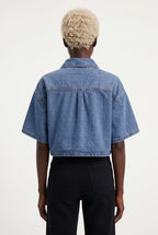 This is a medium-wash denim short-sleeved cropped jacket features a boxy, modern silhouette with relaxed drop shoulders and wide, elbow-length sleeves with stitched turned hems.