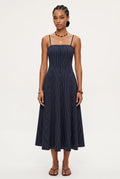 A woman modeling a navy blue midi dress with thin vertical white pinstripes, featuring spaghetti straps and a buttoned bodice, set against a plain light gray studio background.
