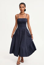 A woman modeling a navy blue midi dress with thin vertical pinstripes, shown from a three-quarters back view against a plain white studio background.