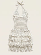 An off-white crocheted halter dress with a tiered fringe skirt, displayed flat against a light beige background.