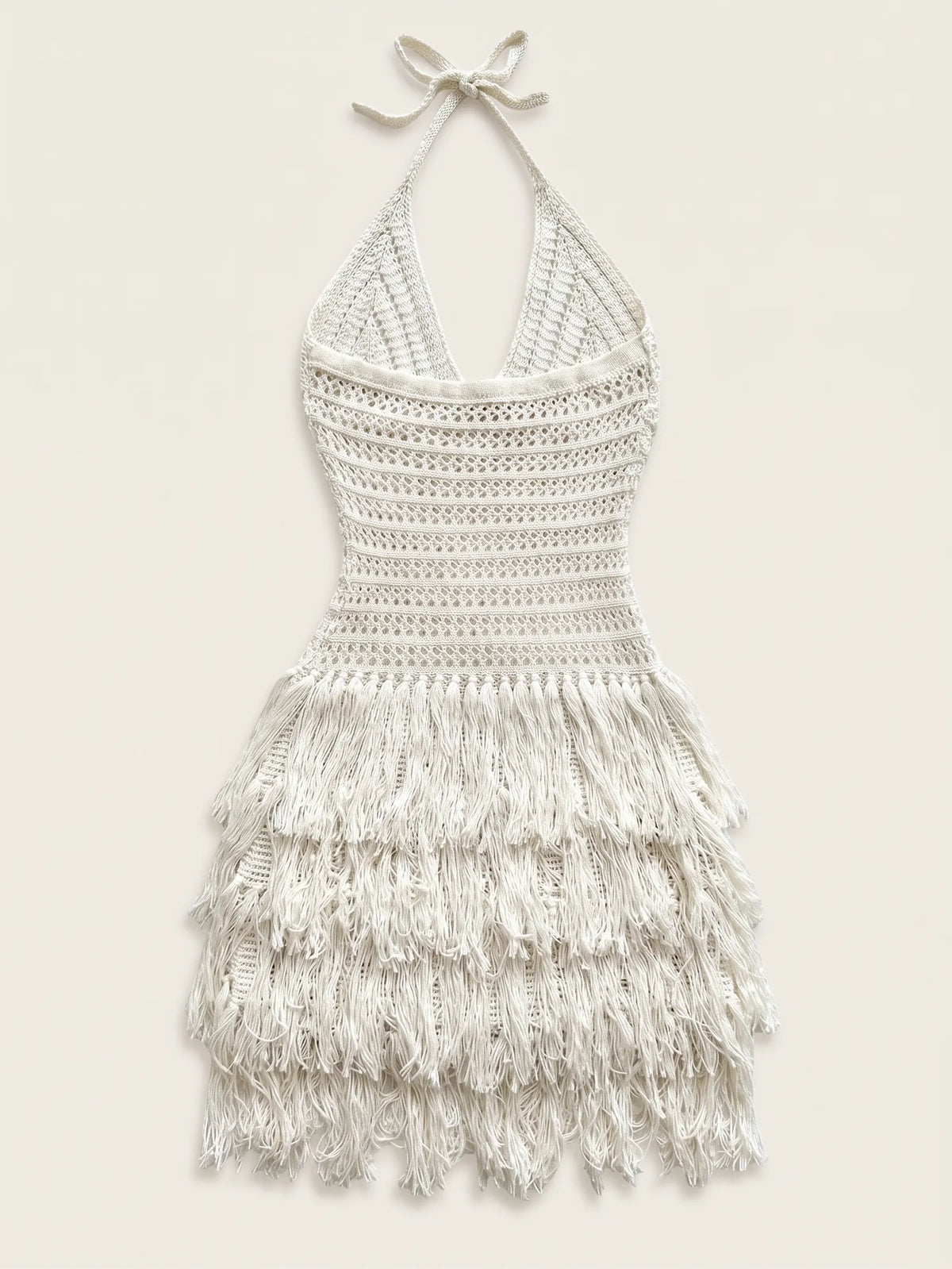 An off-white crocheted halter dress with a tiered fringe skirt, displayed flat against a light beige background.