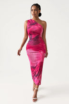 A woman modeling a one-shoulder bodycon midi dress with a vibrant pink and magenta abstract watercolor pattern, paired with white strappy high-heeled sandals against a plain white studio background.