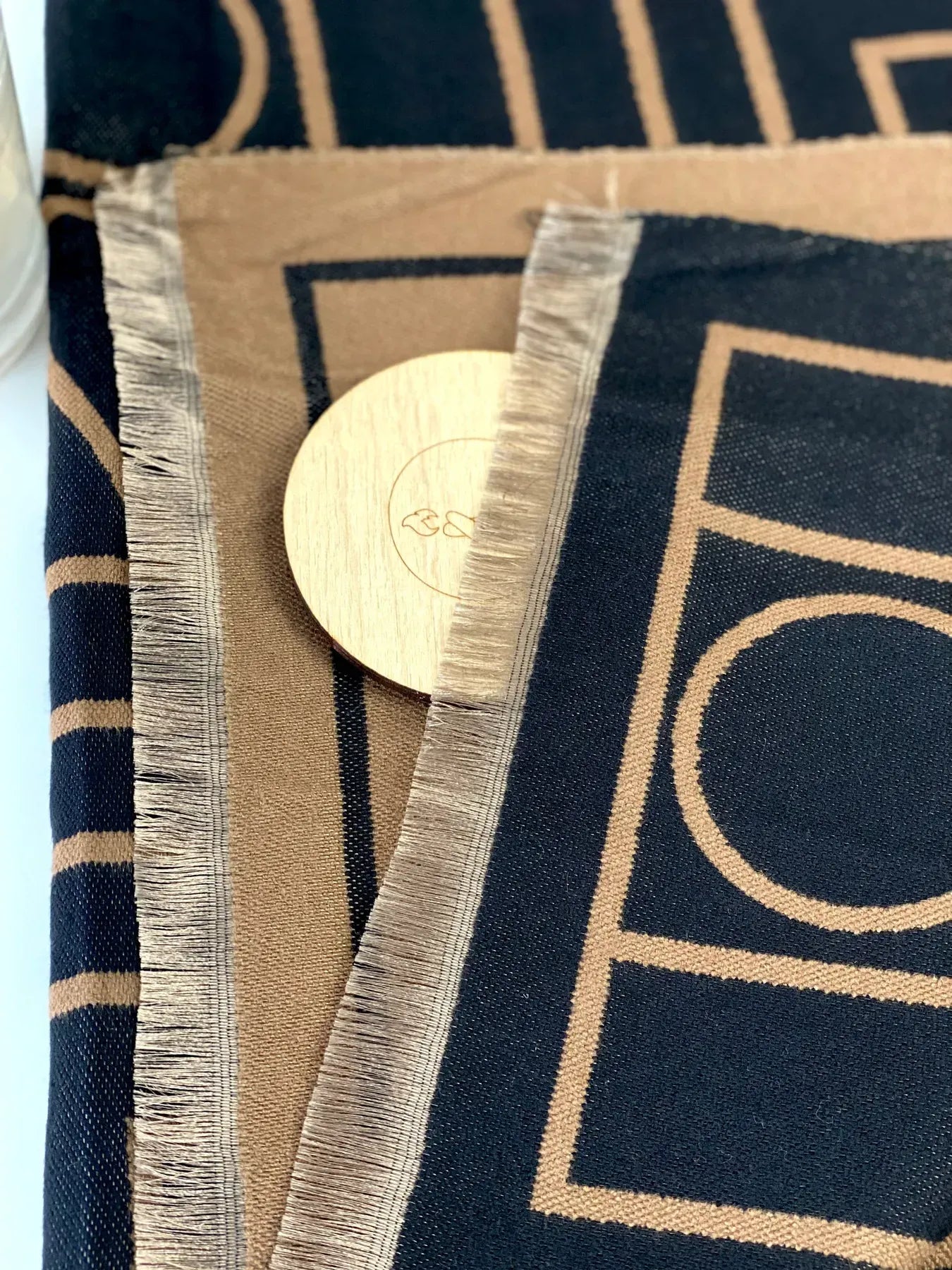 Close-up of a fabric with geometric patterns and a wooden circular object on a blue and beige background.