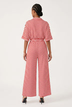 A woman viewed from the back wearing a red and white horizontally striped short-sleeve jumpsuit with a tie waist and wide legs, paired with black heels, against a plain white studio background.