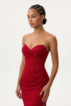 A woman modeling a strapless red gown with a sweetheart neckline, ruched bodice, and gathered skirt against a plain light background.