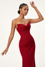A woman modeling a strapless, sweetheart-neckline red evening gown with ruched draping details, posed against a clean white studio background.