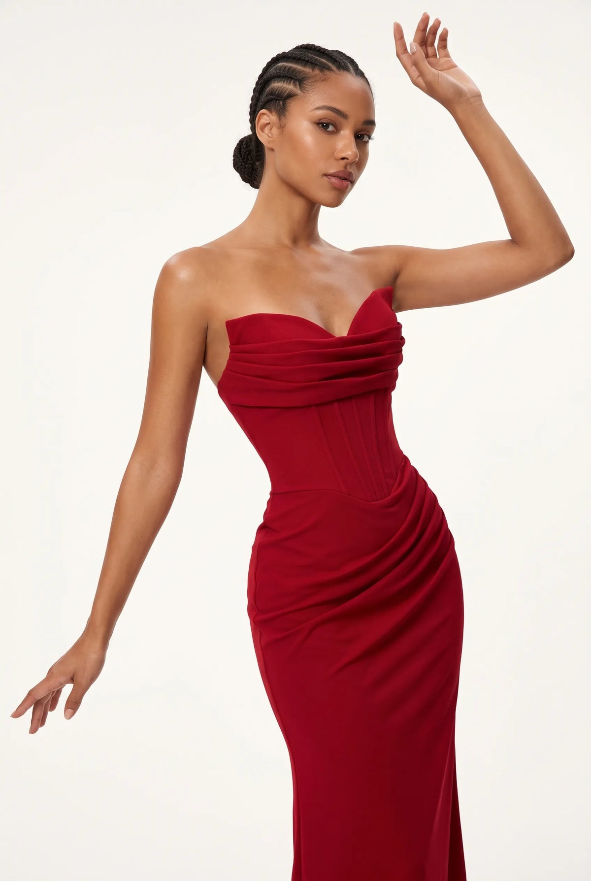 A woman modeling a strapless, sweetheart-neckline red evening gown with ruched draping details, posed against a clean white studio background.