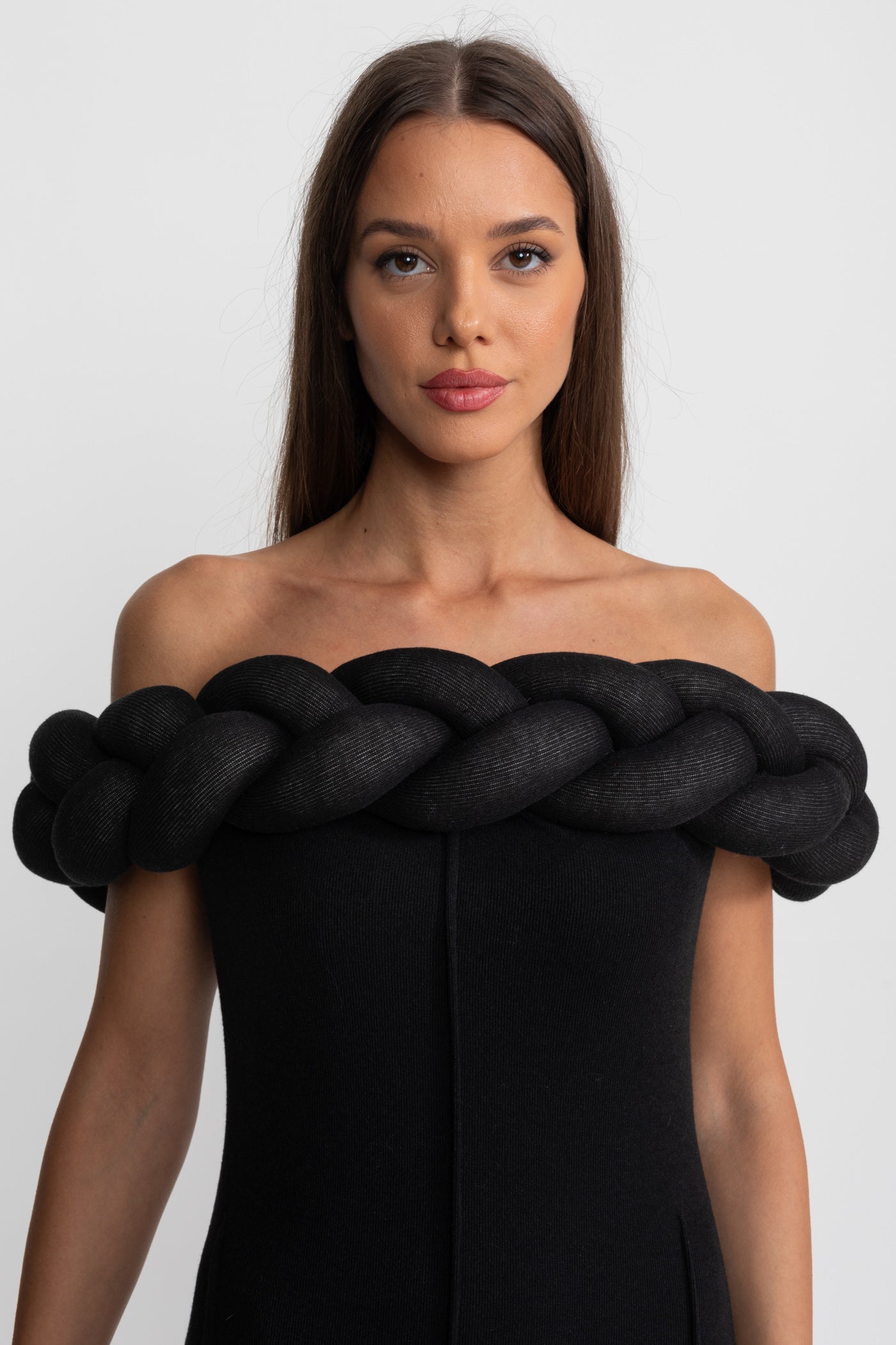 Woman wearing a black strapless dress with large braid detail on a white background