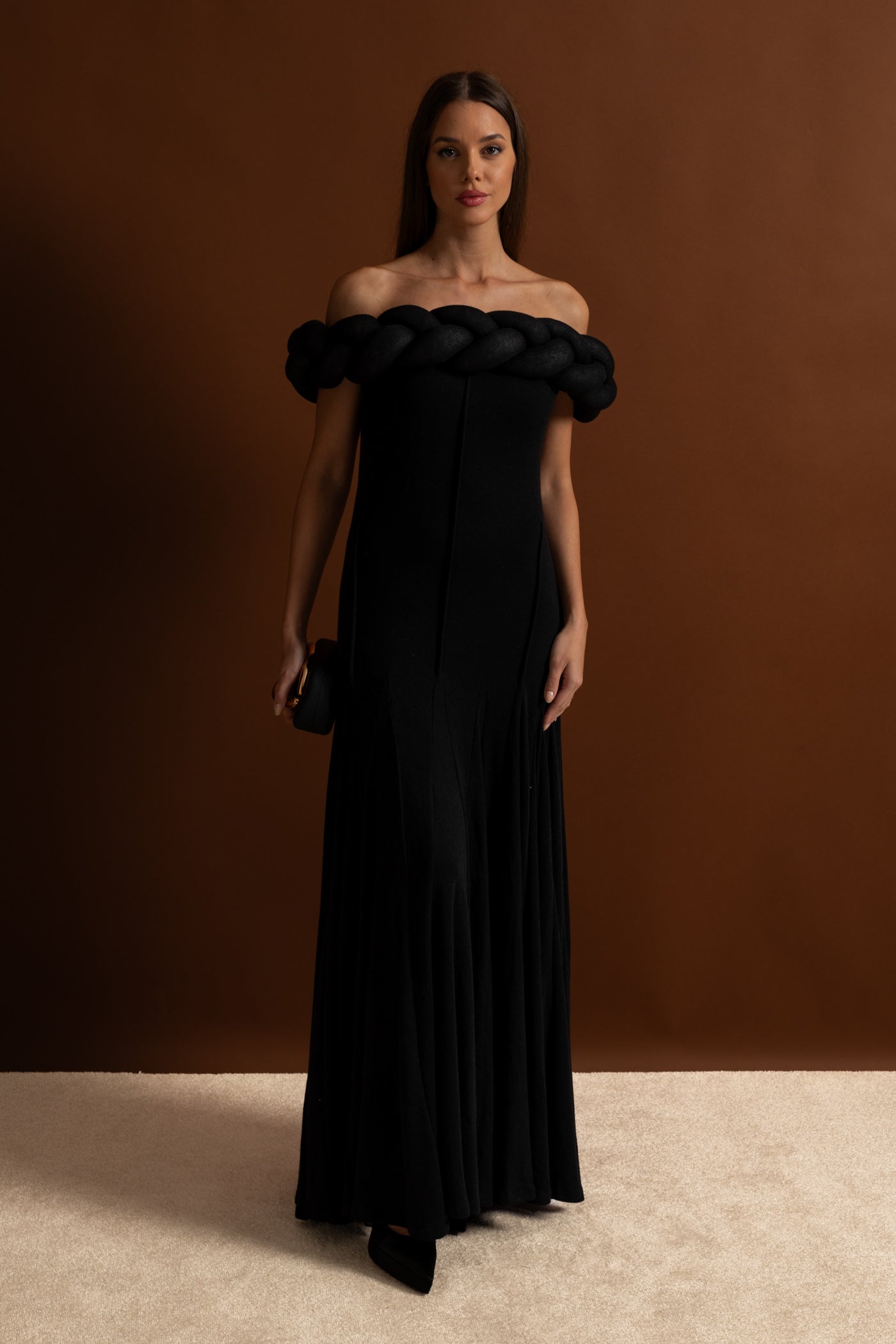 Woman wearing a black off-shoulder gown against a brown background