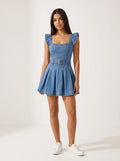 Model wearing a short-sleeved denim mini dress is crafted from a medium-blue wash denim featuring a structured, square-necked bodice with molded, bustier-style seaming and playful ruffled shoulder straps. Designed with a fitted waist cinched by a matching fabric belt with a metallic buckle, the dress flows down into a flared, pleated skater skirt that creates a crisp, youthful silhouette.