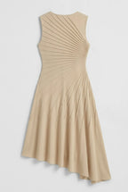This sleeveless, beige midi dress features a crew neckline and a sophisticated sunray pin-tuck design that radiates outward across the fitted bodice. Crafted from a fluid, medium-weight fabric, the dress forms structural pleated lines that extend downward through an A-line silhouette, culminating in a dramatic asymmetrical high-low hemline that flows gracefully around the legs.