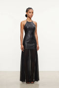 A model stands against a plain white studio background wearing a sleeveless black faux-leather halter top and a long black sheer pleated midi skirt.