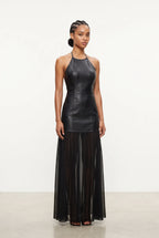 A model stands against a plain white studio background wearing a sleeveless black faux-leather halter top and a long black sheer pleated midi skirt.