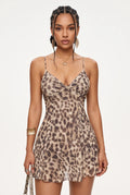 A woman modeling a sleeveless leopard-print mini dress with thin spaghetti straps and a sweetheart neckline, photographed against a clean white studio background.