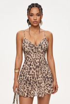 A woman modeling a sleeveless leopard-print mini dress with thin spaghetti straps and a sweetheart neckline, photographed against a clean white studio background.