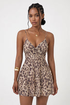 A woman modeling a sleeveless leopard-print mini dress with thin spaghetti straps and a sweetheart neckline, photographed against a clean light gray studio background.