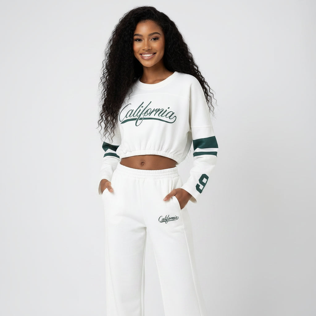 Person wearing a white sweater with green accents and white pants, standing against a plain background.