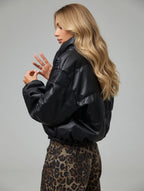 Woman wearing a black leather jacket and leopard print pants on a gray background