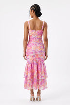 This is a vibrant maxi dress features an all-over abstract watercolor floral print in shades of pink, orange, purple, and yellow on a light background. It is designed with a sweetheart bustier-style top with sweetheart cutout at the center bust, thin shoulder straps, and a front waist cutout.