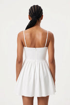 A woman viewed from the back wearing a white spaghetti-strap mini dress with a fitted bodice and flared skirt, against a plain light background.
