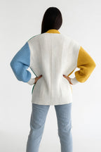 Person wearing a colorful sweater with blue, yellow, and white sleeves on a white background