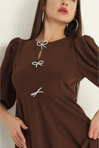 Brown dress with bow details worn by a model against a neutral background